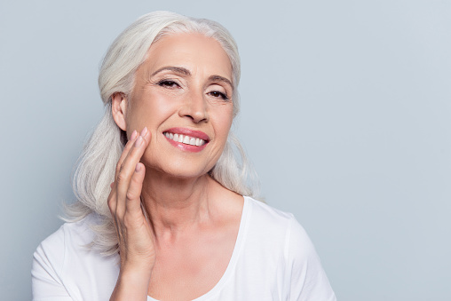 A beautiful mature woman touching her face and showing off her new smile after full mouth reconstruction Premier Dental Center