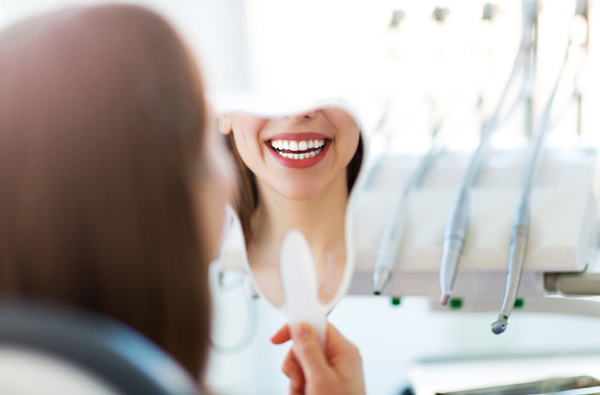 Woman looking at her smile in a mirror after her restorative dentistry procedure at Premier Dental.