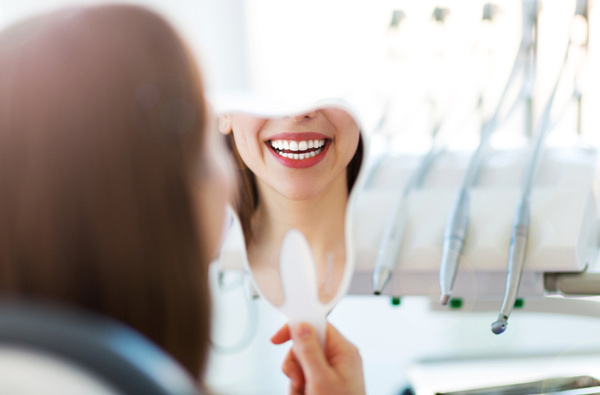 Woman looking at her smile in a mirror after her restorative dentistry procedure at Premier Dental Center. Woman looking at her smile in a mirror after her restorative dentistry procedure at Premier Dental Center.