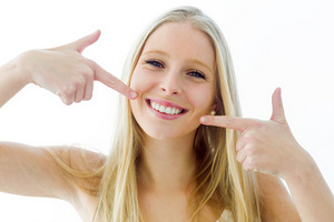 A blonde woman pointing at her white teeth at Premier Dental.